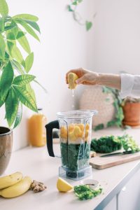 Woman squeezing lemon into a blender fulled with fruit and veg