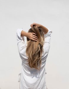 Blond woman wearing white shirt facing white wall